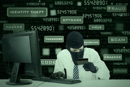 Internet Theft - businessman wearing a mask and holding a credit card while sat behind a computer