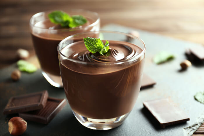 Schokopudding im Glas mit einem Stück Schokolade daneben.