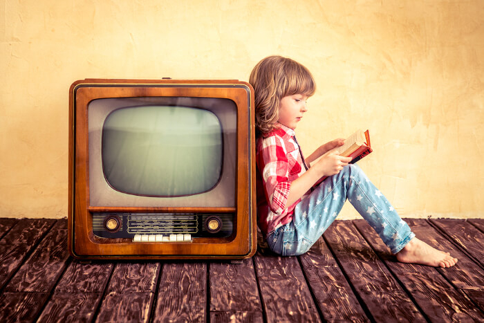 Kleines Kind liest neben Fernseher ein Buch