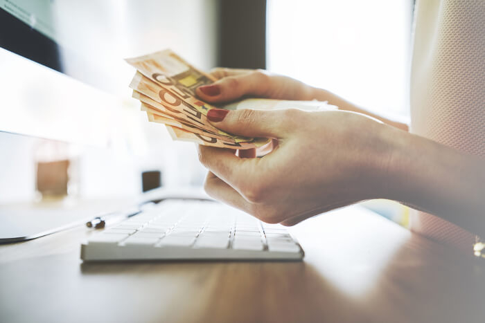 Frau hält Geldscheine vor ihrem Rechner in den Händen