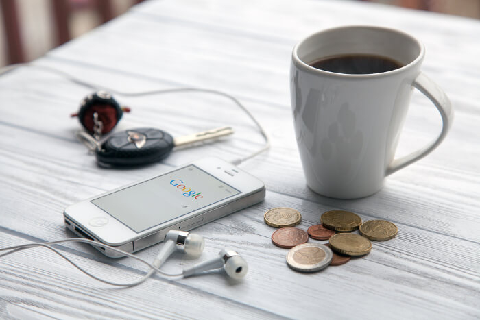 Smartphone mit Google-Loge auf Tisch - daneben Münzen
