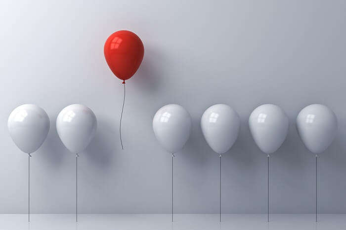 Ein roter Ballon neben vielen weißen
