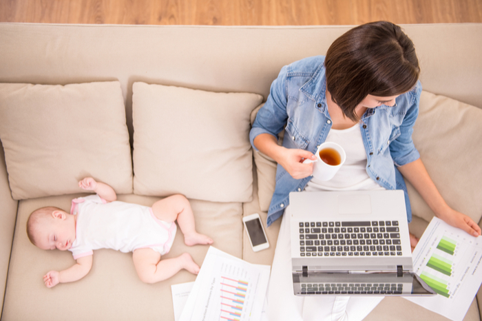 Baby mit arbeitender Mutter auf der Couch