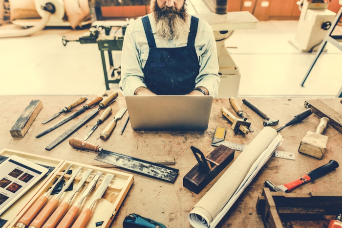 Handwerker sitzt an einem mit Werkzeug beladenen Tisch am Laptop