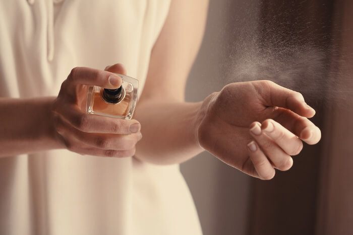 Frau, die sich Parfüm auf das Handgelenk sprüht.
