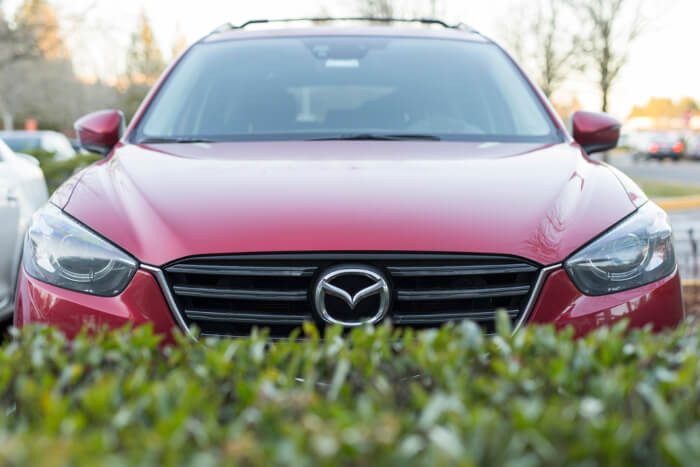 Auto des Herstellers Mazda hinter einer Hecke