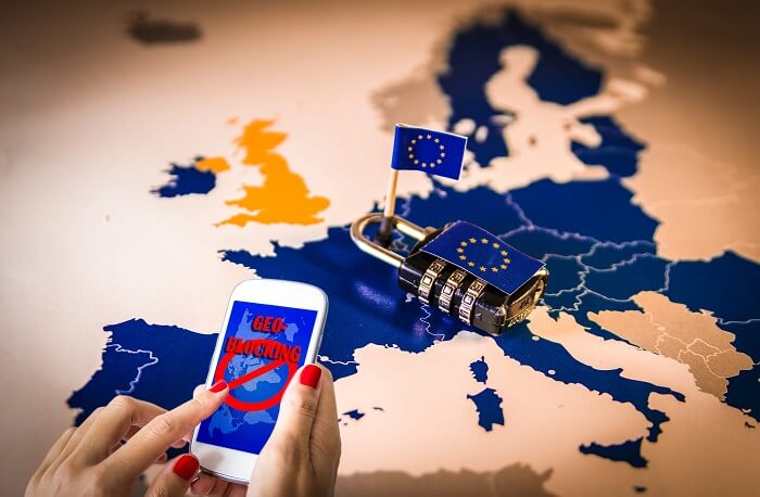 Frauenhände halten ein Smartphone mit einer durch Geoblocking blockierten Seite. Im Hintergrund eine Karte der EU mit einem Zahlenschloss.