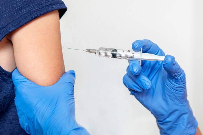 Mensch mit Handschuhen spritzt Impfung in Arm