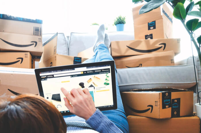 Person tippt auf Tablet vor Amazon-Paketen