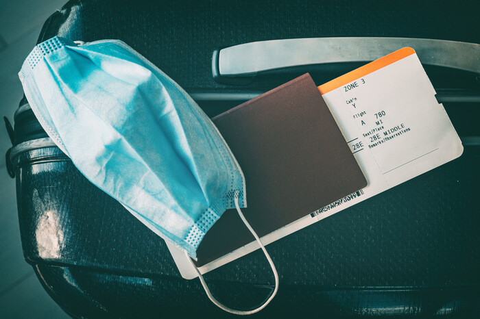 Maske und Reisepass mit Flugticket liegen auf Koffer