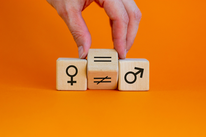 Symbol für die Gleichstellung der Geschlechter. Die Hand dreht einen Würfel und ändert ein ungleiches Zeichen zu einem gleichen Zeichen zwischen den Symbolen von Männern und Frauen. 