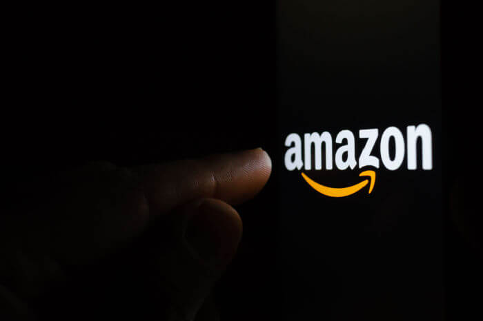 Finger berührt Amazon-Logo dunkler Hintergrund