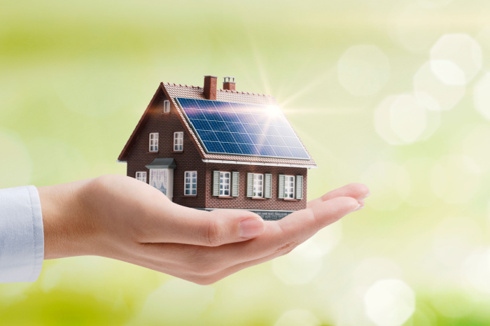Hand hält Einfamilienhaus mit Solaranlage