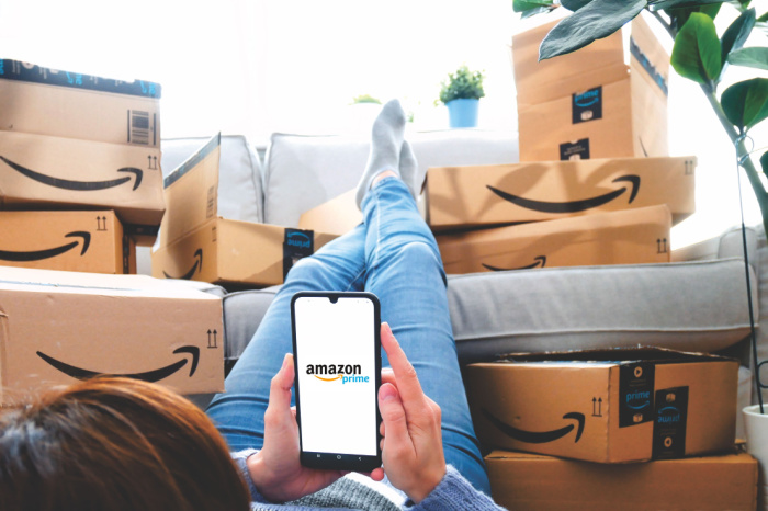 Amazon-Pakete auf Sofa und Person, die Amazon-App auf Handy öffnet