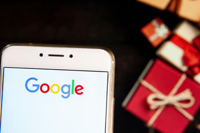 Google-Logo auf Smartphone, Weihnachtsgeschenke im Hintergrund
