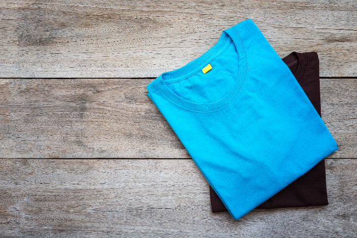 Ein blaues und ein schwarzes T-Shirt, die zusammen gefaltet auf einem Holzuntergrund liegen. 