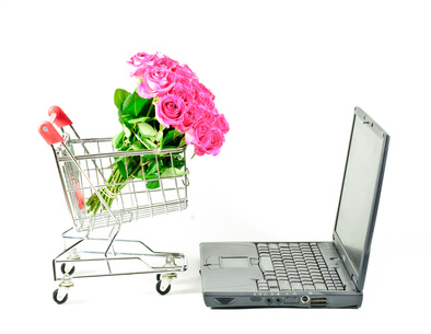 Laptop mit Blumenstrauß im Einkaufswagen