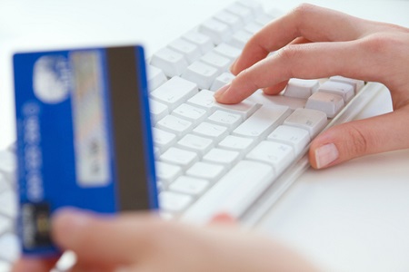Frauenhand an Tastatur, eine Hand hält Kreditkarte 