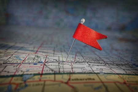 Closeup of a pin with red flag stuck in a map 