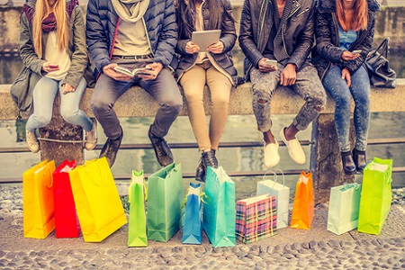 Gruppe von Freunden sitzt auf Bank mit Shopping-Bags, mit Smartphones in der Hand